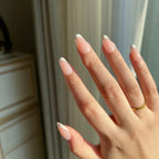 Hand with LuxeTip French short oval nails in pink color and a gold ring against a neutral background