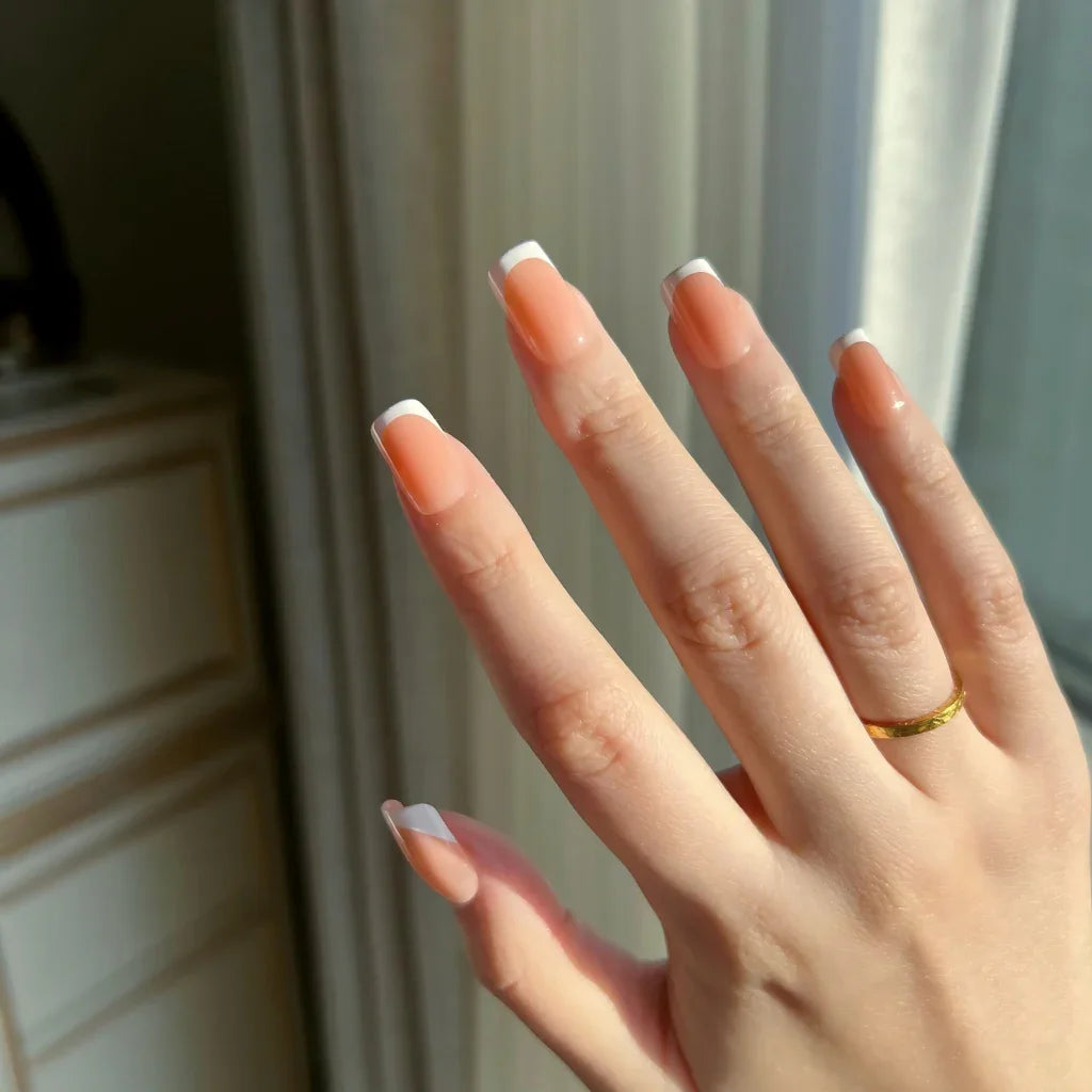 Hand with LuxeTip French short square press-on nails in light brown color  and a gold ring in front of a neutral background