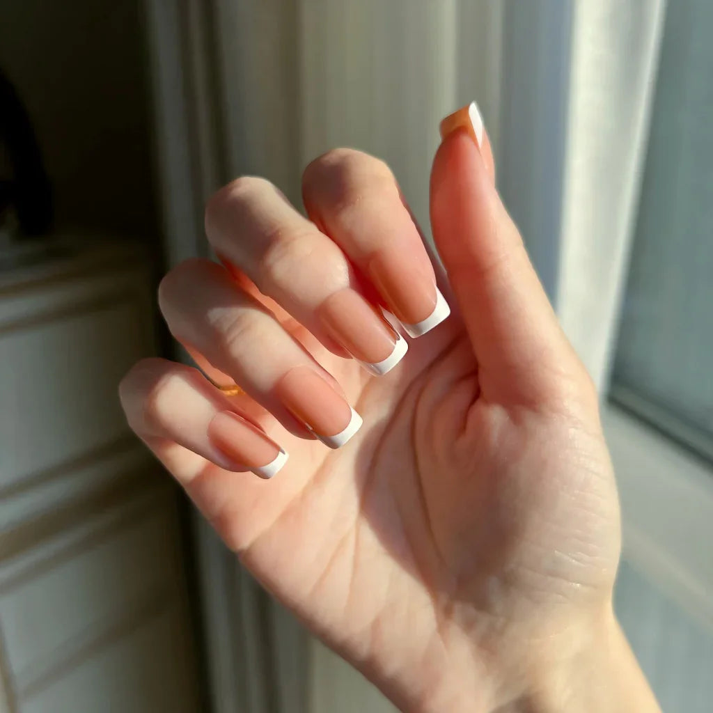 Hand with LuxeTip French short square press-on nails in light brown color in a neutral setting