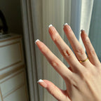 Close-up of a hand with LuxeTip French short square press-on nails in mocha color and a gold ring, blurred background