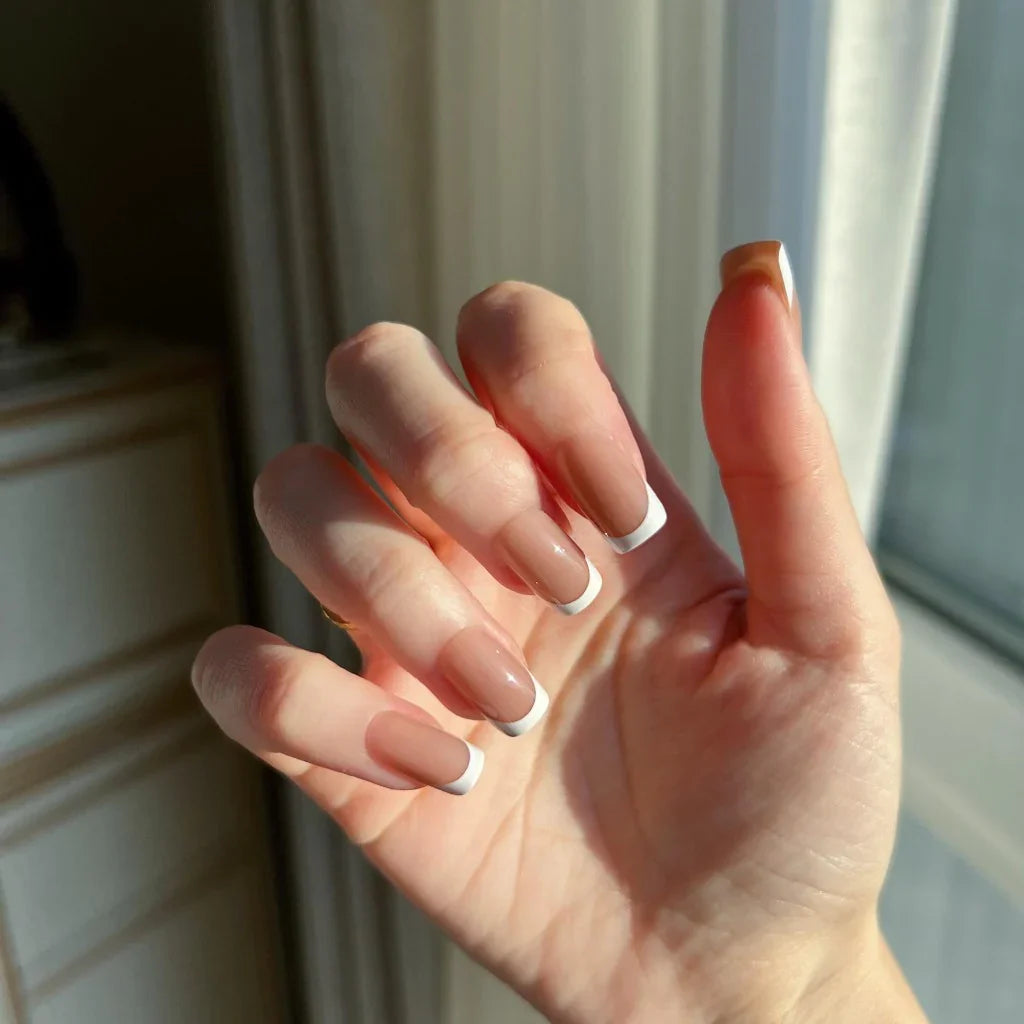Hand with LuxeTip French short square press-on nails in mocha color in front of a window
