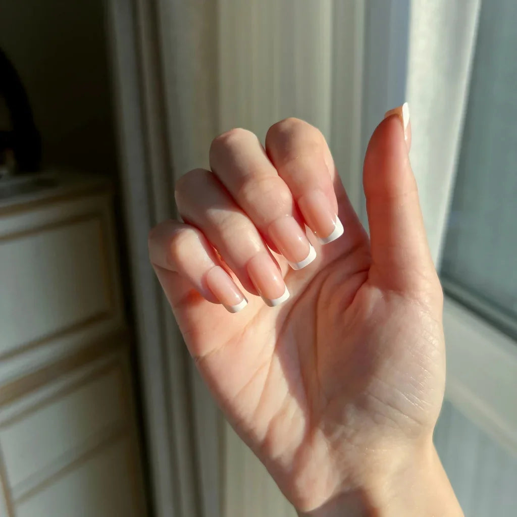 Hand with LuxeTip French short square press-on nails in peach color in front of a window