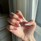 Close-up of a hand with LuxeTip Glazed French medium almond nails with light brown color in front of a window.