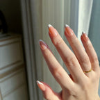 Close-up of a hand with LuxeTips Glazed short almond nails in light brown and a gold ring, blurred background