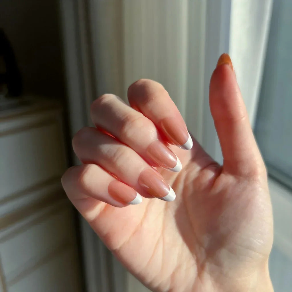 Close-up of one hand wearing LuxeCharm LuxeTip glazed French Short Almond press on nails in light brown color.  In the neutral background