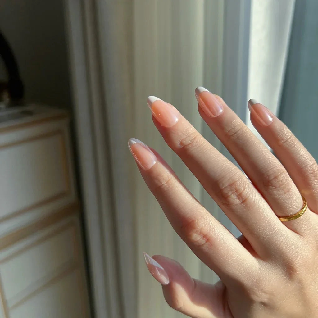 Hand wearing LuxeCharm LuxeTip glazed French Short Almond press on nails in peach color. In front of a neutral background