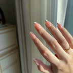 Hand wearing LuxeCharm LuxeTip glazed French Short Almond press on nails in peach color. In front of a neutral background
