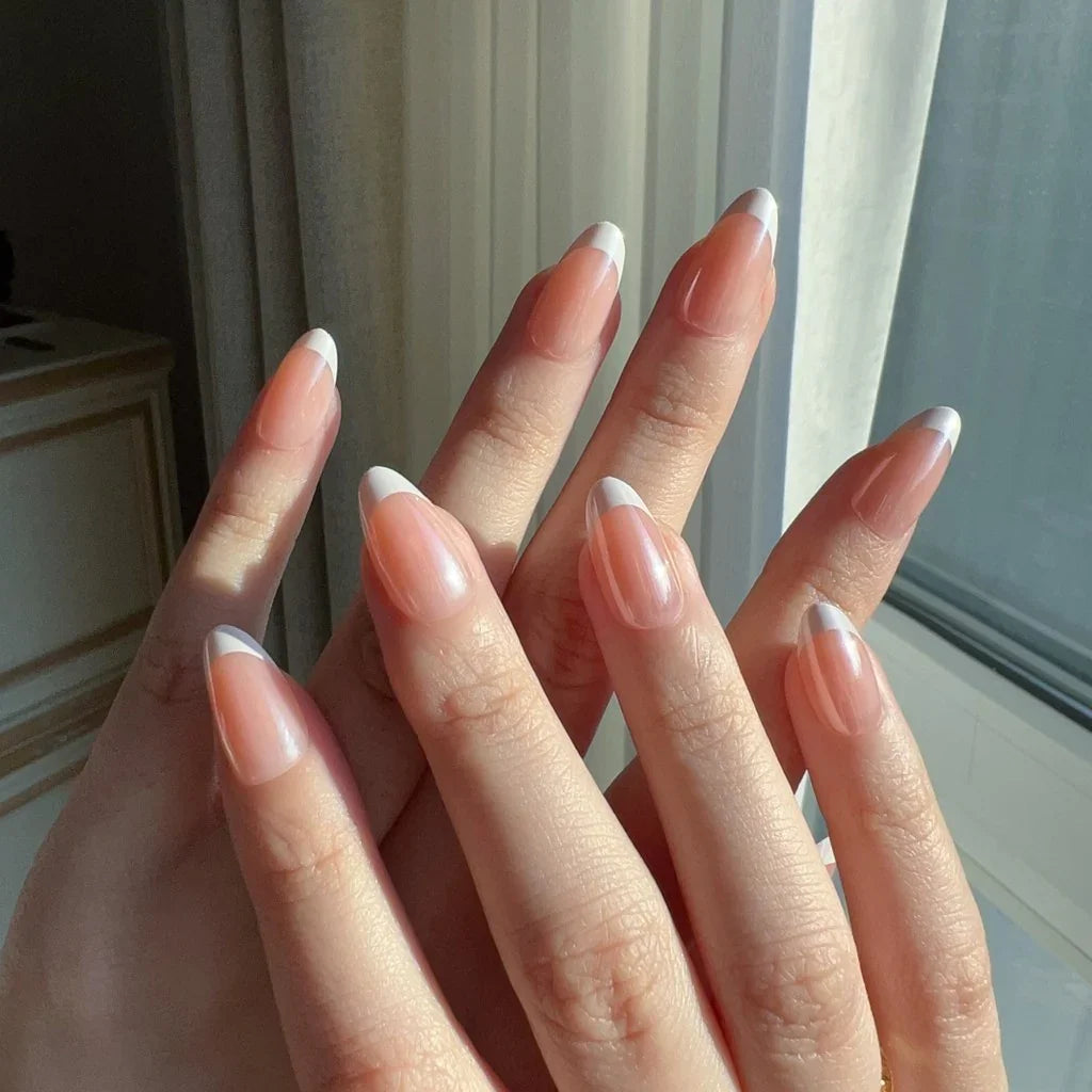 Close-up of hands wearing LuxeCharm LuxeTip glazed French Short Almond press on nails in peach color. 