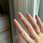 Hand with LuxeTip Glazed French short square nails with light brown color and a gold ring against a neutral background
