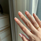 Close-up of hands wearing LuxeCharm LuxeTip glazed French Short Square press on nails in peach color. 