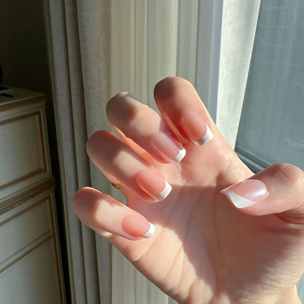 Hand withLuxeTip Glazed French short square nails with peach color in front of a window with curtains