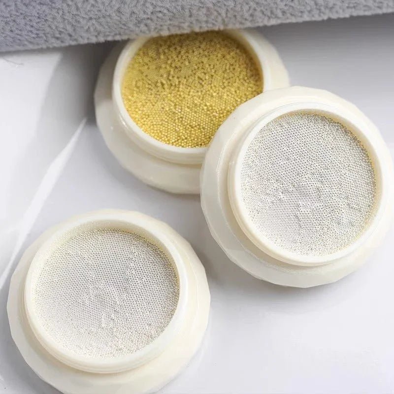 Three small containers with different gold and silver mini metal beads on a white surface. LuxeCharm