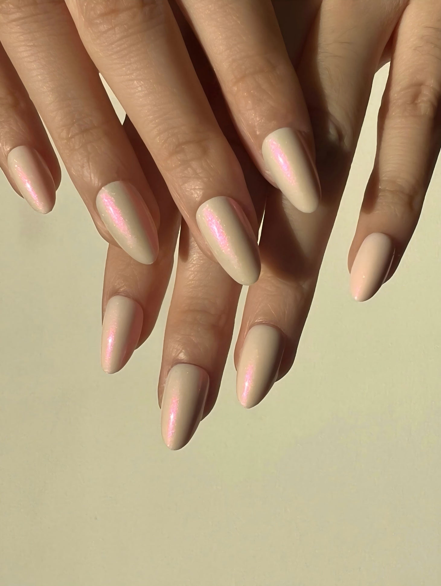 Close-up of hands with LuxeCharm Opal Haze Aurora Nails, Short Almond nails on a beige background