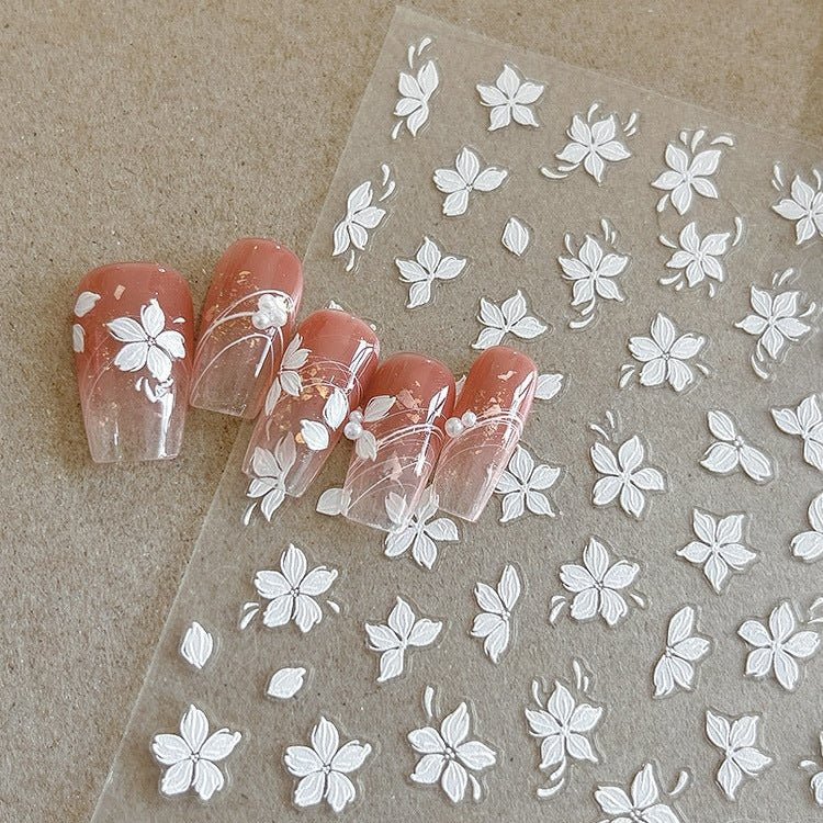 Nail art stickers with white floral designs on a clear sheet, next to a set of nails with similar design. LuxeCharm nail stickers