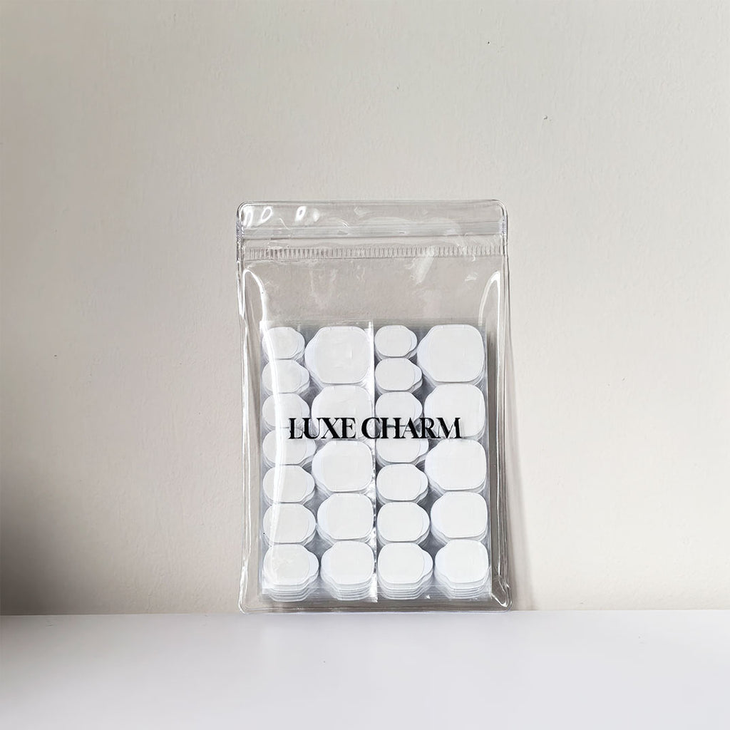 Clear plastic bag with LuxeCharm logo-sticky tabs inside the bag. item is against a light gray background