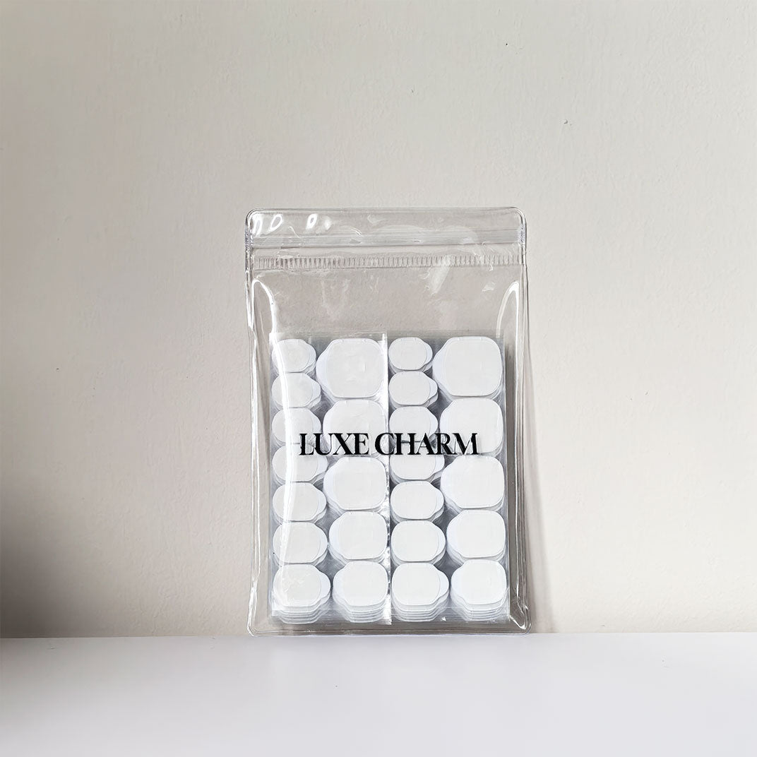 Clear plastic bag with LuxeCharm logo-sticky tabs inside the bag. item is against a light gray background