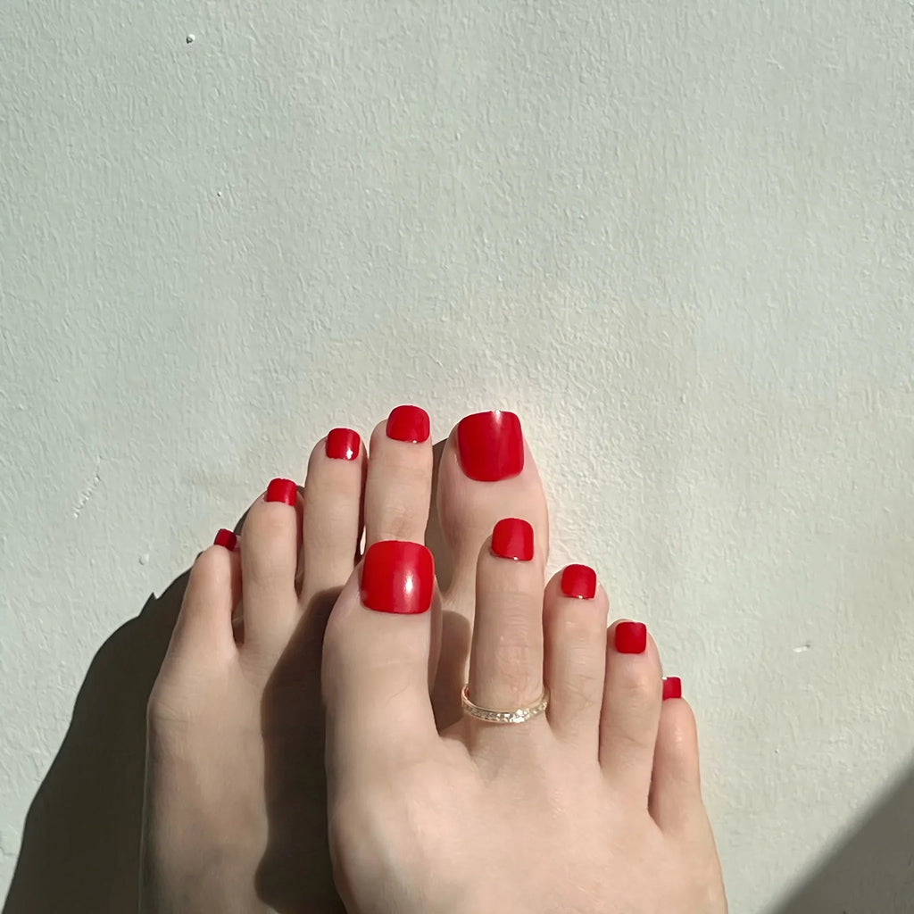 Close-up of toes with red toenails on a light gray background. LuxeCharm toenails