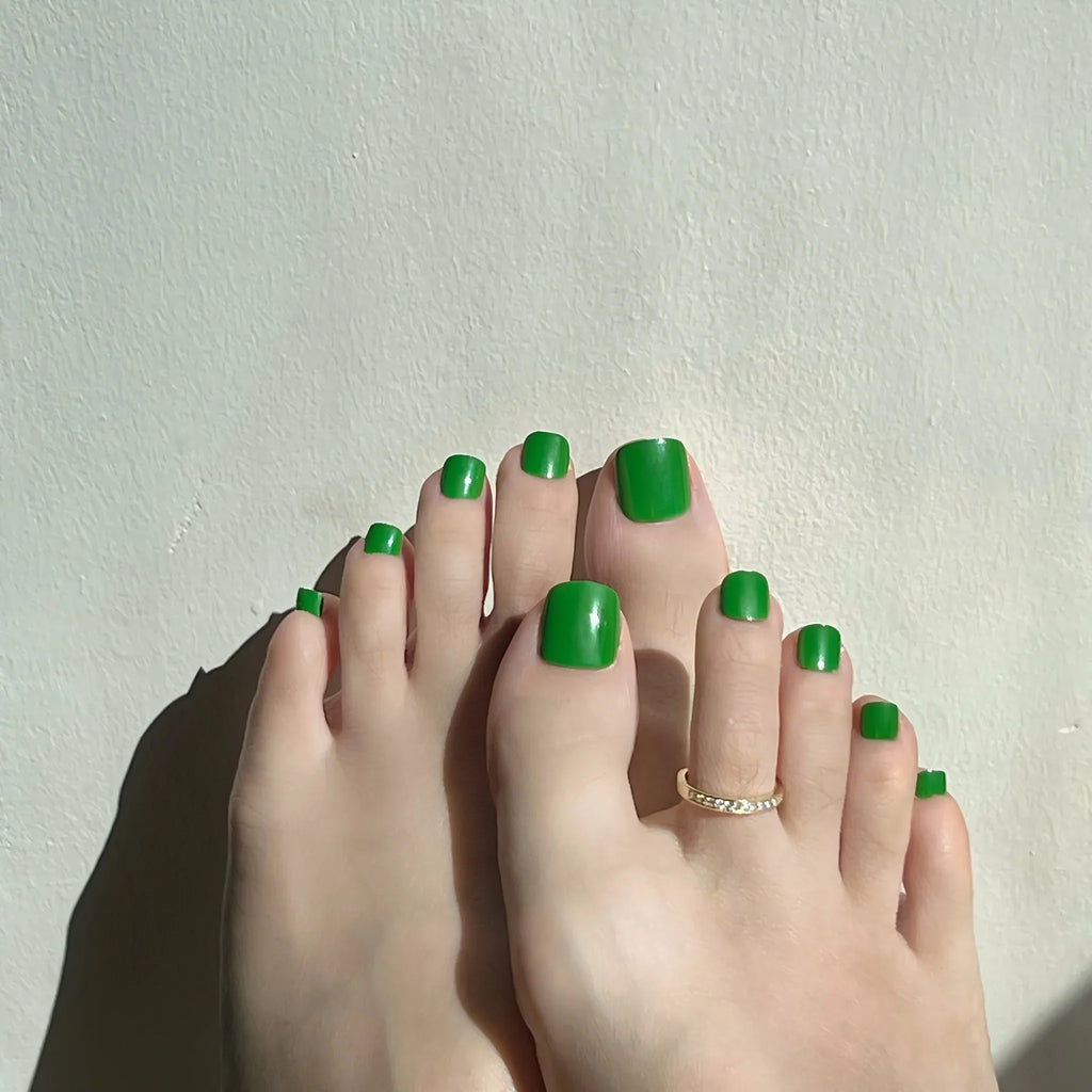 Feet with green emerald press on toenails on a light background. LuxeCharm toenails