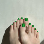 Feet with green emerald press on toenails on a light background. LuxeCharm toenails