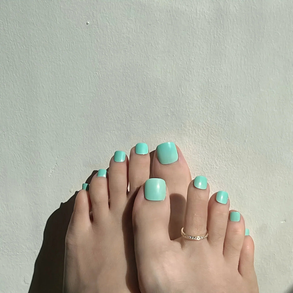 Toes with mint press on toenails on a light gray background. LuxeCharm toenails