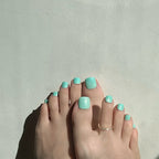 Toes with mint press on toenails on a light gray background. LuxeCharm toenails