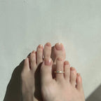 Close-up of a foot wearing sand press on toenails and  a gold toe ring on a light background. LuxeCharm toenails