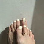 Close-up of a feet with vanilla press on toenails on the toes against a neutral background. LuxeCharm toenails
