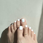 Close-up of feet with white press on toenails on toes against a light gray background. LuxeCharm toenails
